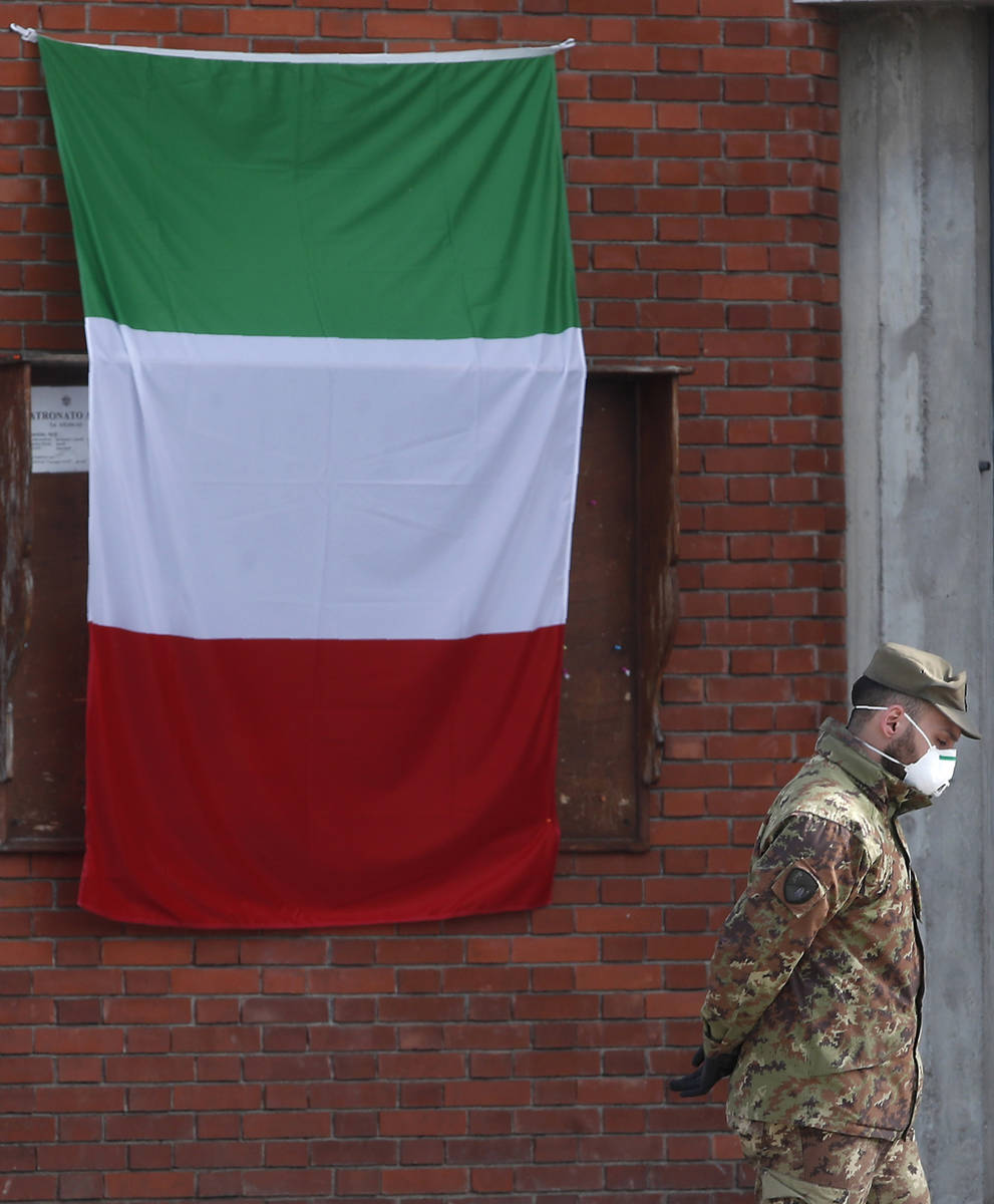 An Italian flag hangs outside the San Giuseppe church as an Army soldier walks past trucks wait ...
