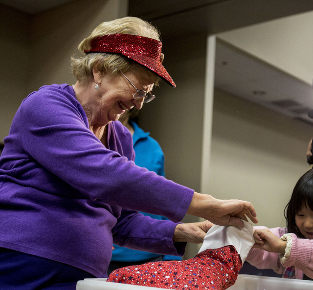 Sharon Brune, a volunteer during the 8th annual &quot;Stockings for our Troops,&quot; holds a stocking while a student from Gordon McCaw Elementary School fills it with candy for active tr ...