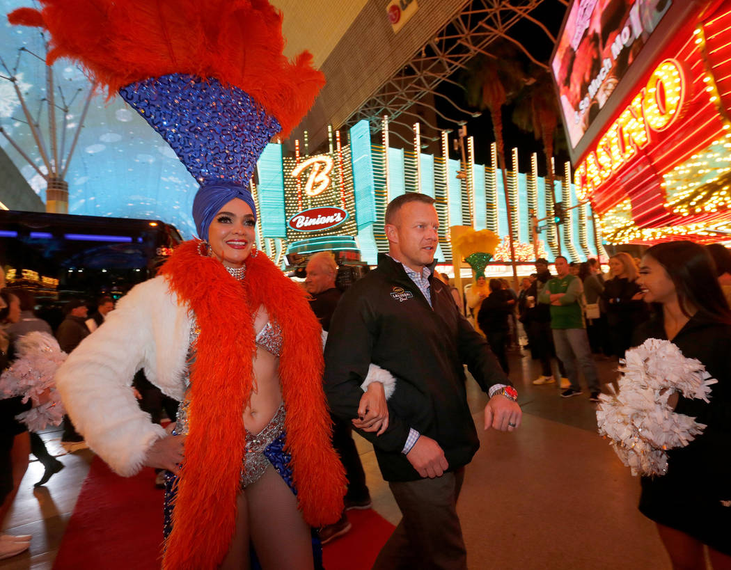 A showgirl escorts Boise State Broncos head coach Bryan Harsin to the Las Vegas Bowl welcome reception at Fremont Street Experience in Las Vegas, Wednesday, Dec. 13, 2017, as Harsin and his team a ...