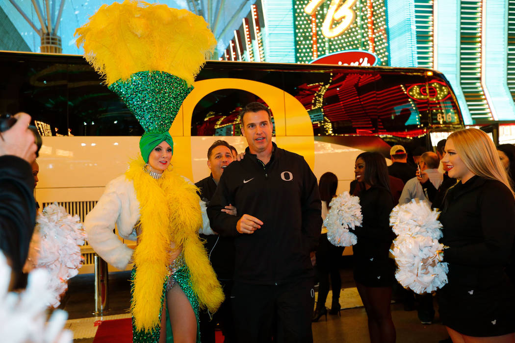 A showgirl escorts Oregon Ducks head coach Mario Cristobal to the Las Vegas Bowl welcome reception at Fremont Street Experience in Las Vegas, Wednesday, Dec. 13, 2017, as Cristobal and his team ar ...