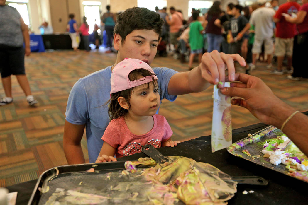 Javier Barra, 18, holds his niece Mia Taliercio, 2, complete their bookmark at the Children's Museum booth at the annual Back to School Fair organized by the Happy Face Foundation at Springs Prese ...