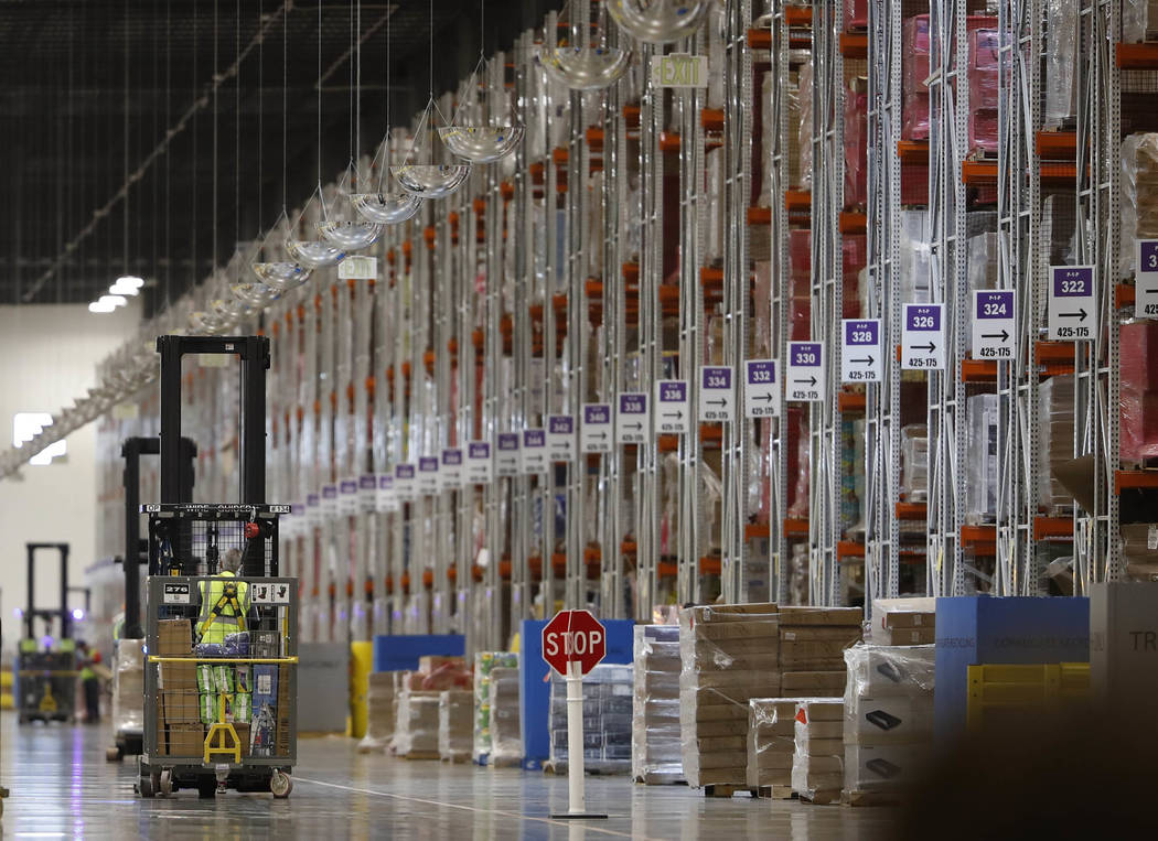 An associate guides a vehicle past rows of goods during a tour of the Amazon fulfillment center ...