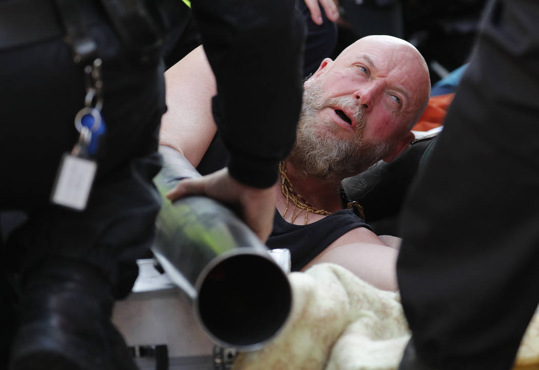 Police attempt to get the hands of a protestor out of a pipe at Oxford Circus in London, Friday ...