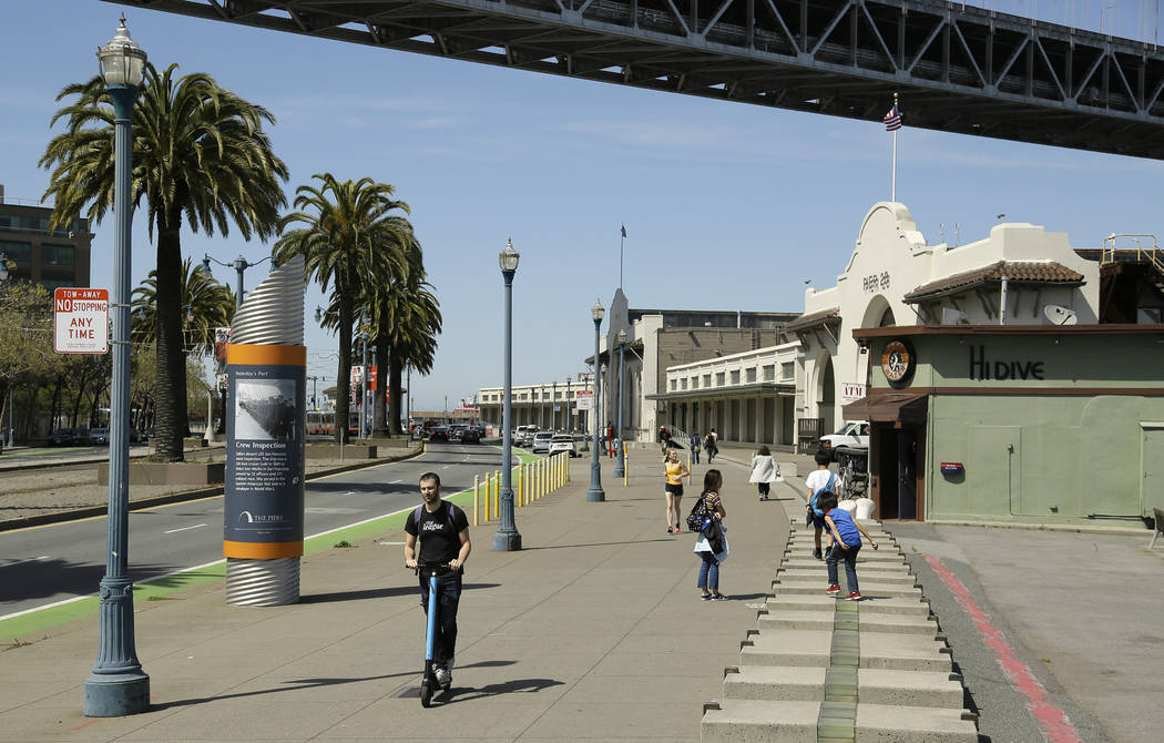 In this photo taken Thursday, April 18, 2019, a man rides a scooter and children play along the ...