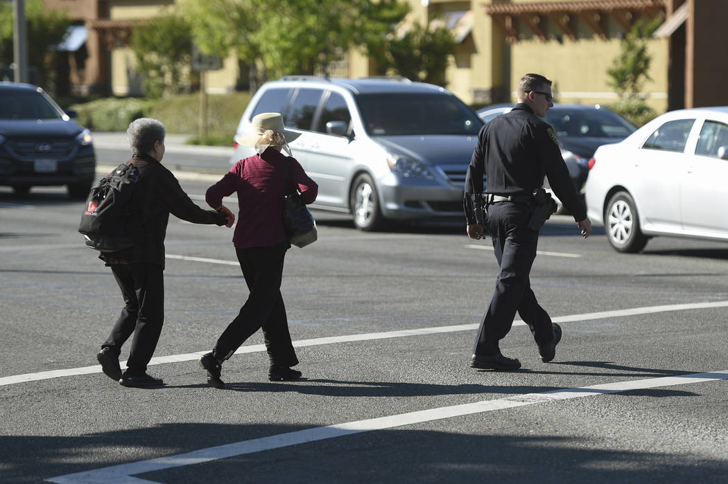 A police officer escorts pedestrians across El Camino Real near the scene of car crash at the i ...