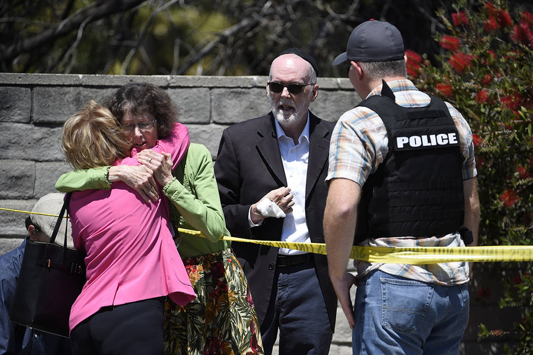 Two people hug as another talks to a San Diego County Sheriff's deputy outside of the Chabad of ...