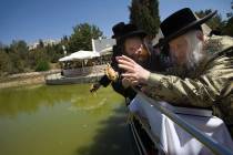 Menachem Mendel Taub, a prominent Hasidic rabbi, right, throws a piece of bread into the water ...