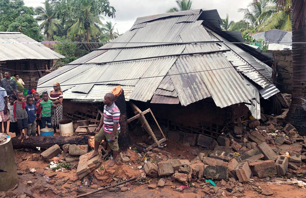 Community members stand near a house where a woman died when her home collapsed due to flooding ...