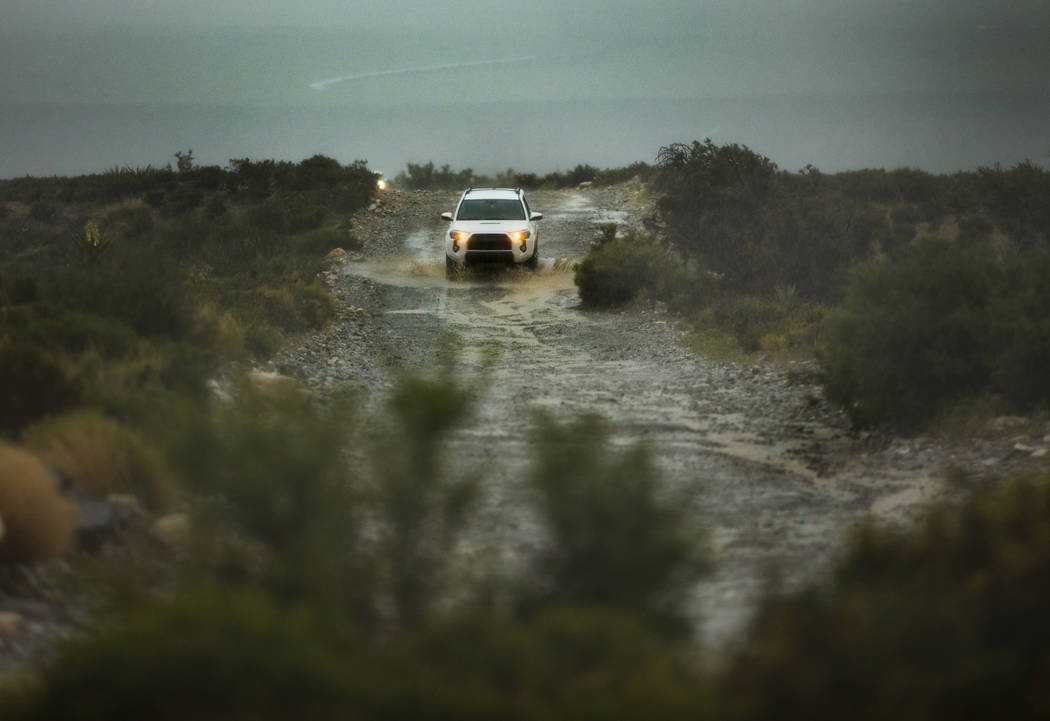 Visitors brave a rain-soaked gravel road as a fast-moving storm makes its way through the Red R ...