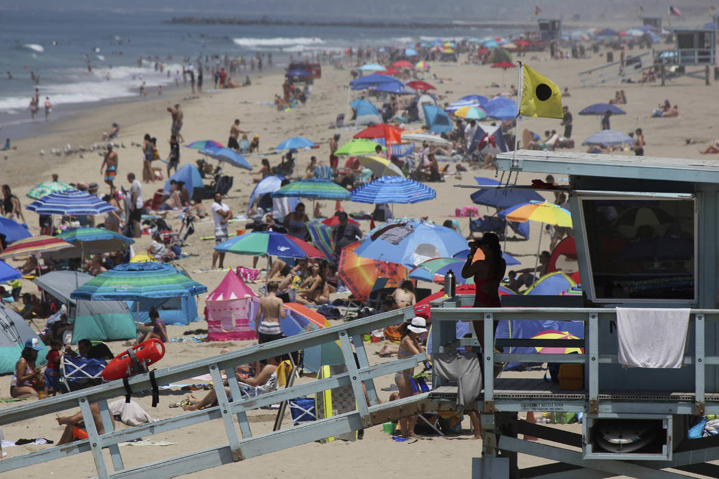 In this July 8, 2017 file photo a lifeguard scans a crowded shoreline at Manhattan Beach, Calif ...