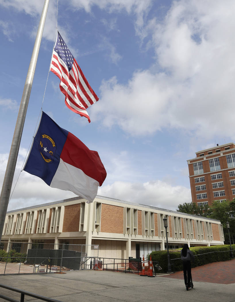 A man rides a scooter past flags at half staff at the University of North Carolina-Charlotte in ...