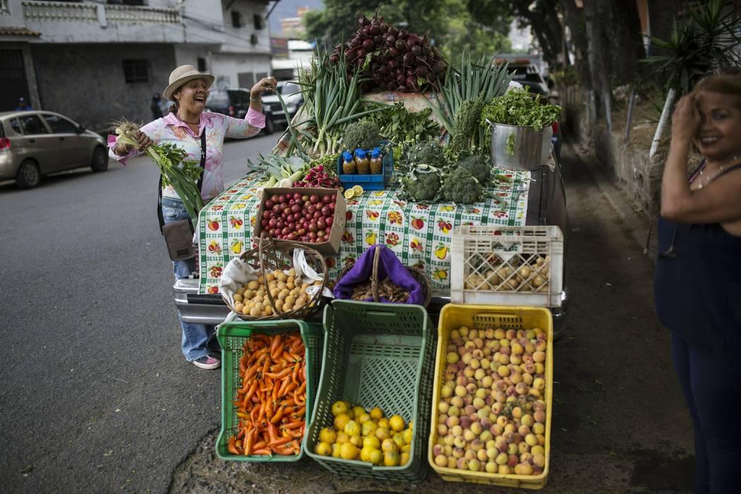 Nancy Espinoza, 55, who uses an old car as her stand, sells vegetables to a customer in Caracas ...