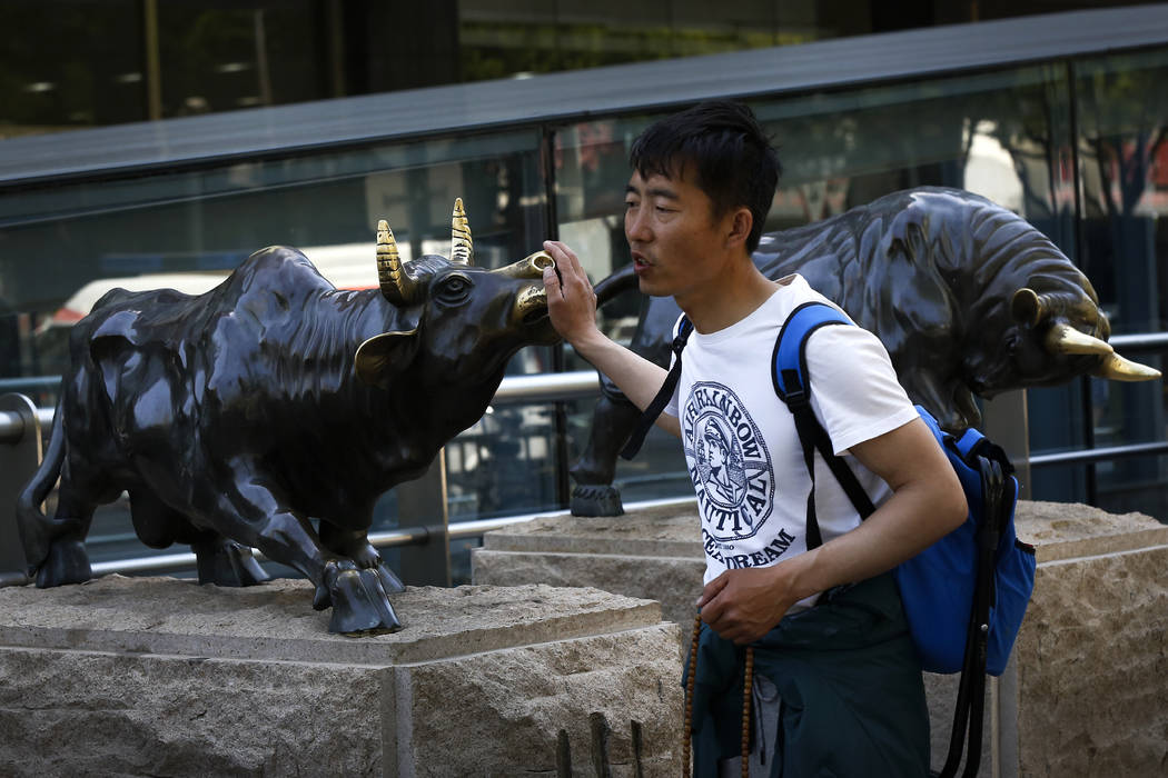 A man touches a bull statue on display outside a bank in Beijing, Monday, May 6, 2019. Shares a ...