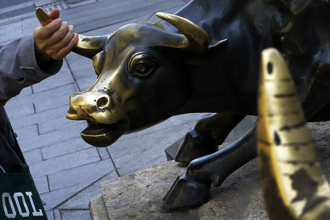 A woman touches a bull statue on display outside a bank in Beijing, Monday, May 6, 2019. Shares ...