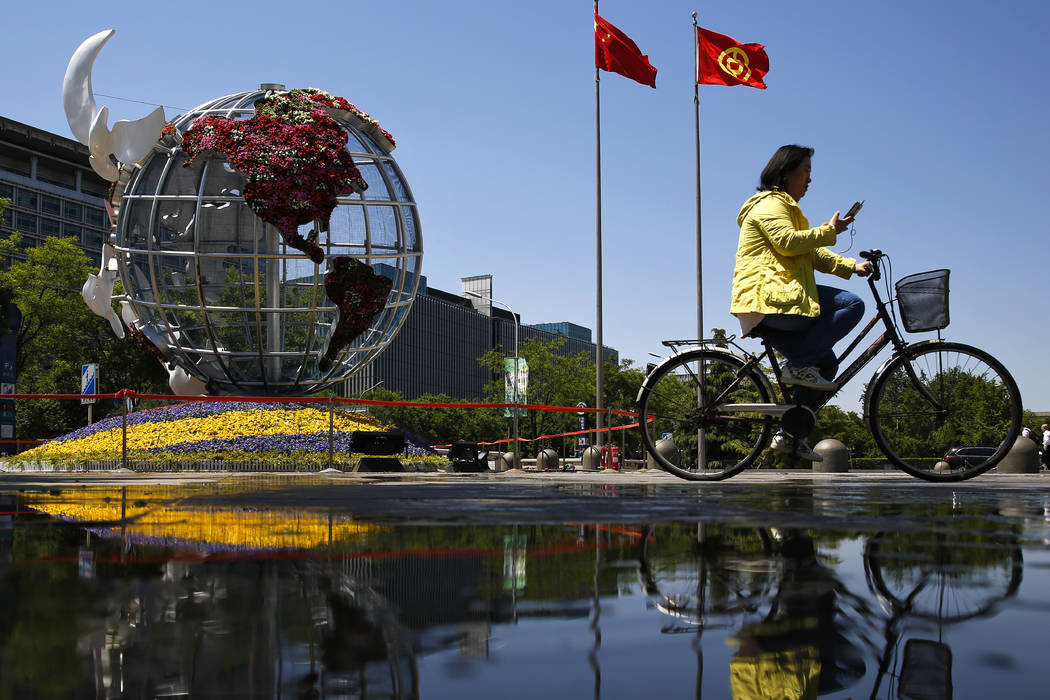 A woman rides a bicycle past a globe structure on display outside a bank in Beijing, Monday, Ma ...