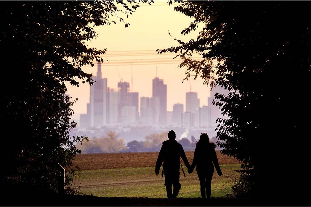 A couple walks through a forest with the Frankfurt skyline in background near Frankfurt, German ...