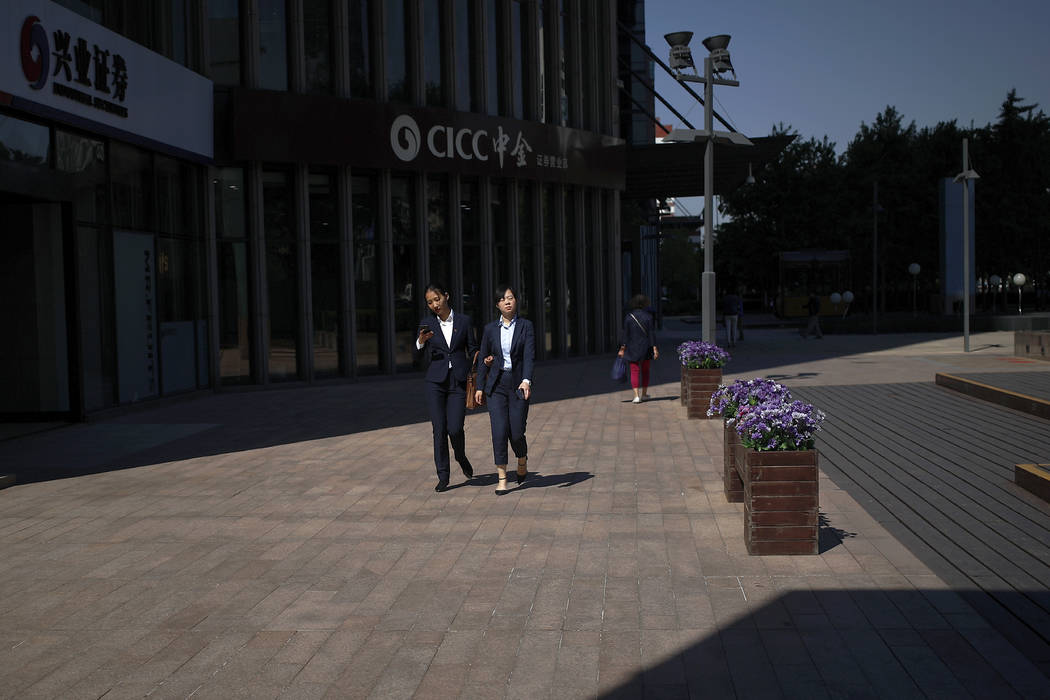 The sunlight is cast on women as they walk by a brokerage house in Beijing, Tuesday, May 7, 201 ...