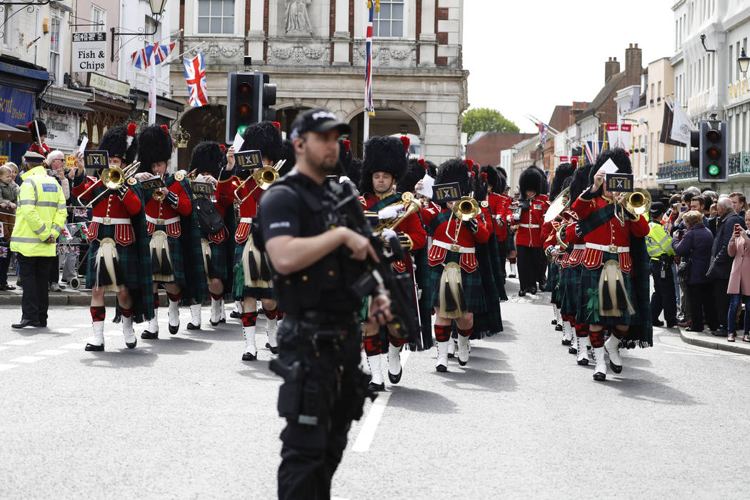 Armed police stand guard as the Royal Regiment of Scotland band march by, on the high street, i ...