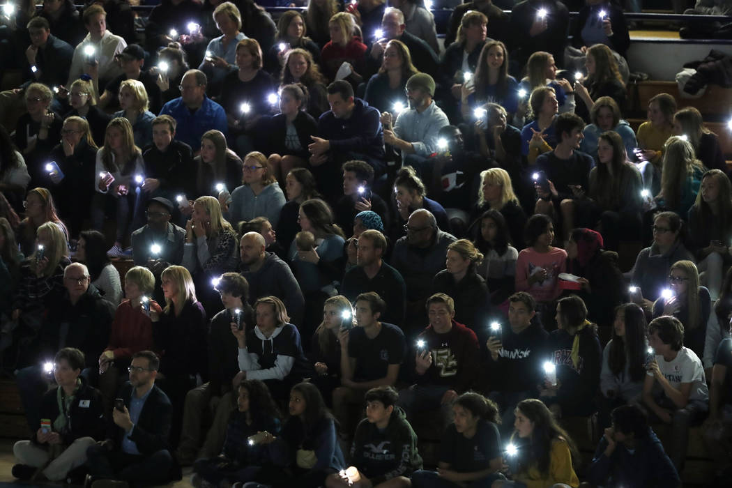 Attendees illuminate their mobile telephones during a community vigil to honor the victims and ...