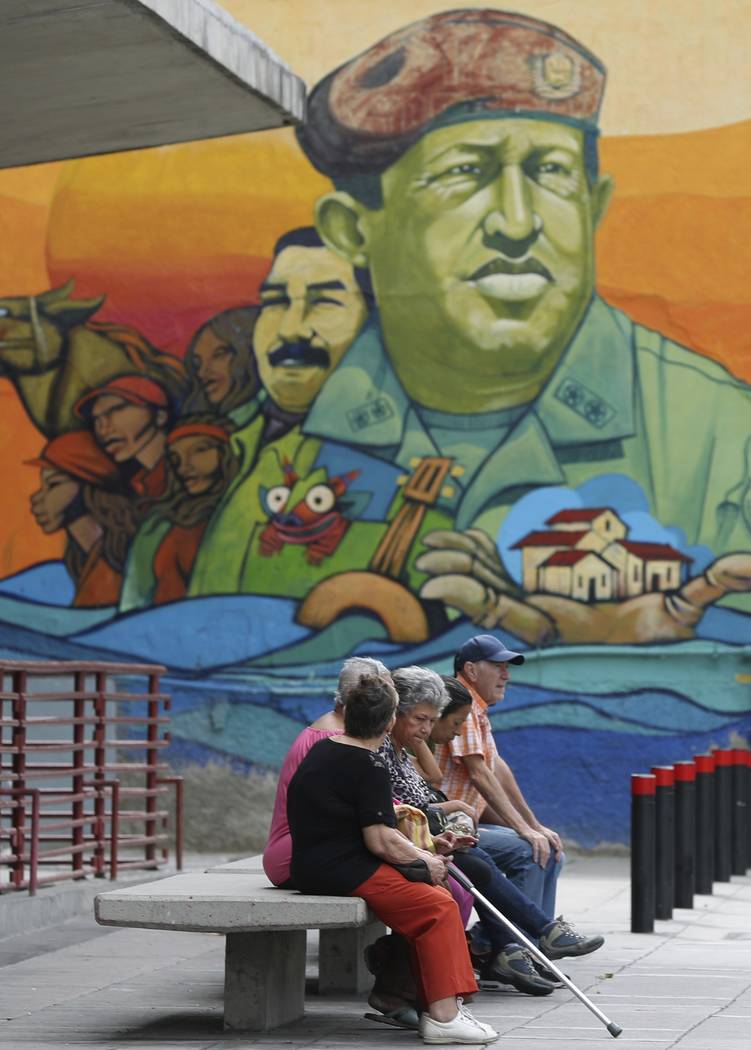 Residents rest on a bench backdropped by a mural featuring Venezuela's late President Hugo Chav ...