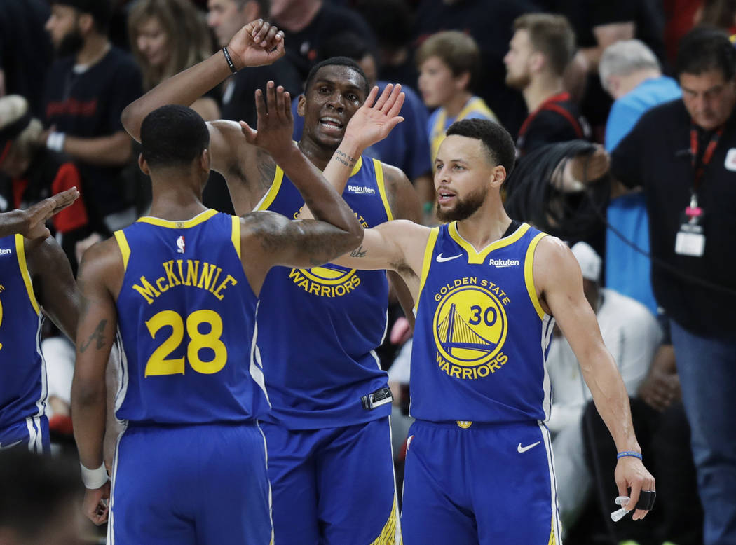 Golden State Warriors guard Stephen Curry, right, greets Alfonzo McKinnie (28) and Kevon Looney ...