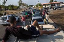 People line the street with their vehicles as they wait to fill up with gas at a fuel station, ...