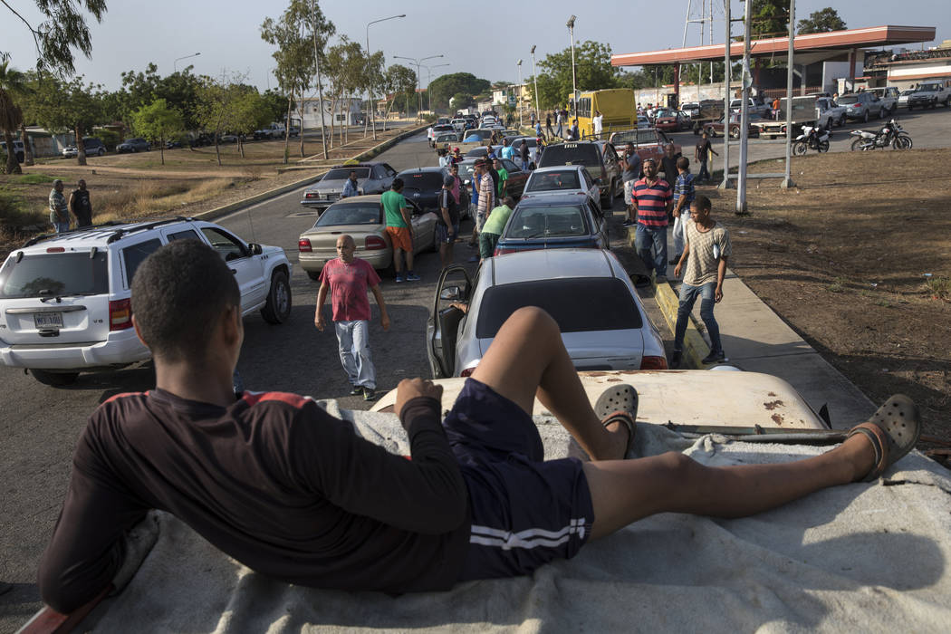 People line the street with their vehicles as they wait to fill up with gas at a fuel station, ...