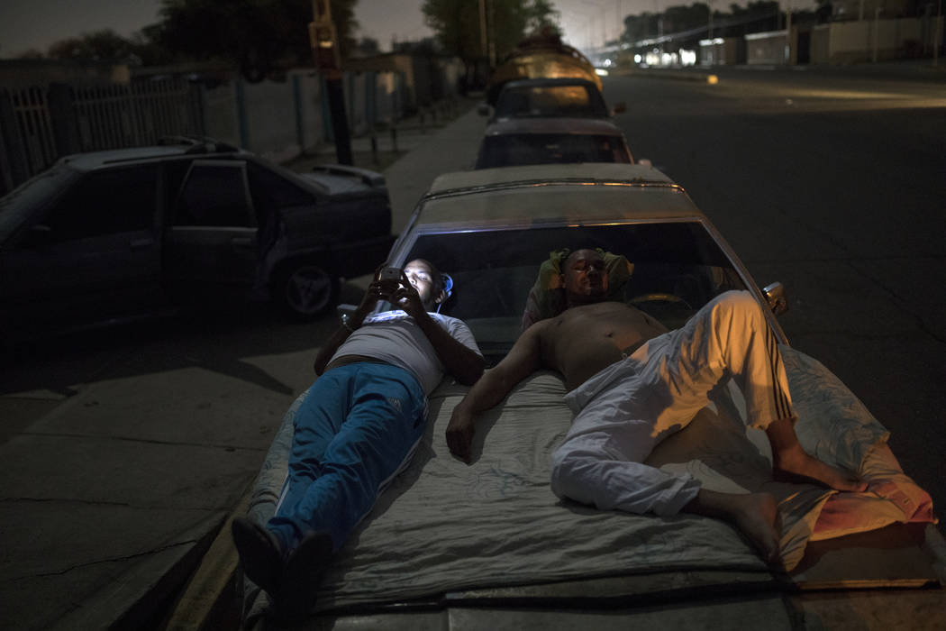 Andres Quintero, left, and Fermin Perez rest on top of Perez's car as they wait in line for ove ...