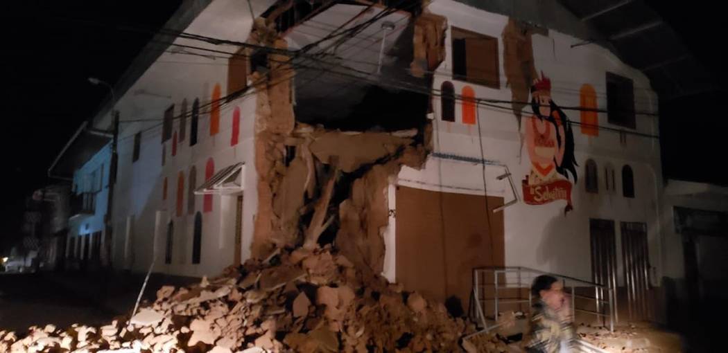 In this photo provided by Firefighters of Peru, people pass in front destroyed wall in Yurimagu ...