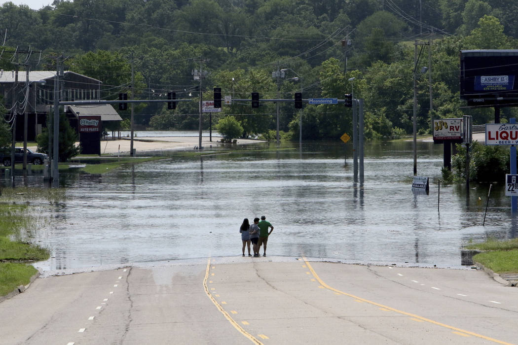 People stand in the middle of Rogers Avenue and look out over the flooded Massard Creek at the ...