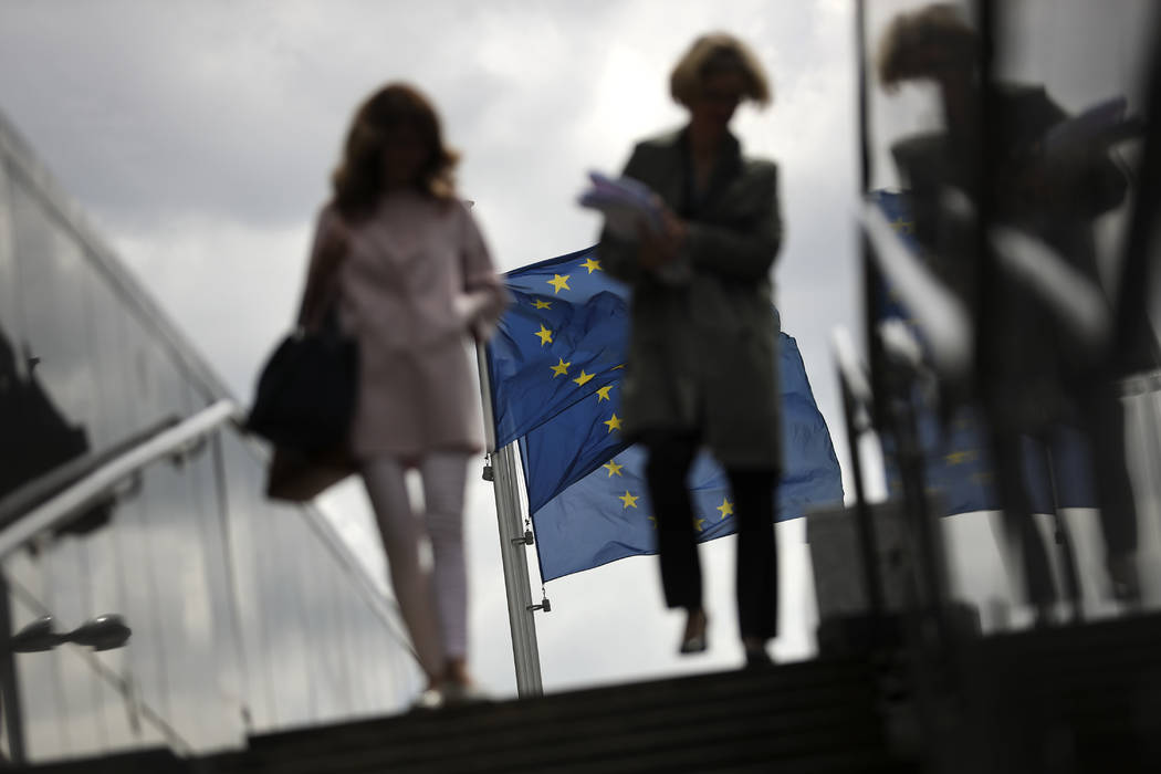 Two women walk near EU flags outside the European Commission headquarters in Brussels, Monday, ...