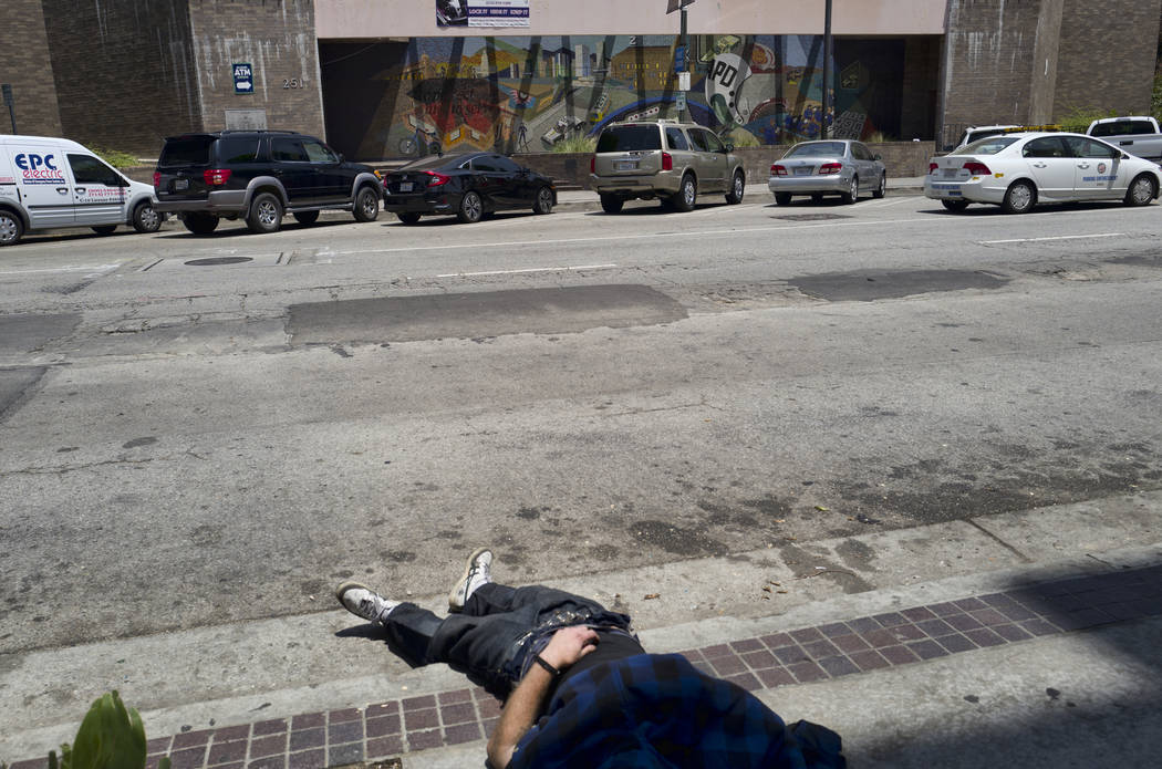 A homeless man sleeps on a curb across the street from LAPD Central Community Police Station in ...