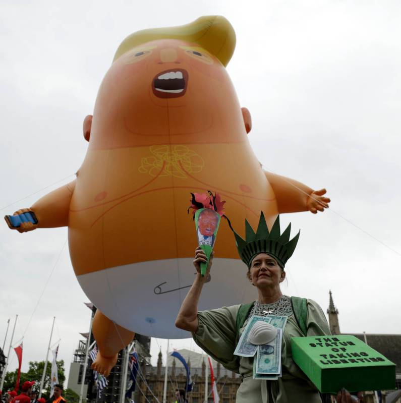 A woman posing as statue of liberty stands next to the 'Trump Baby' blimp as people gather to d ...