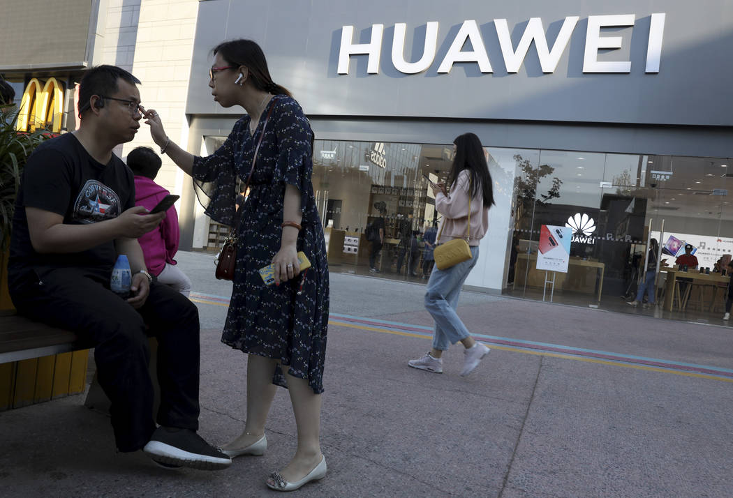 A woman adjusts the glasses of a man outside a Huawei store on May 20, 2019, in Beijing. The wo ...