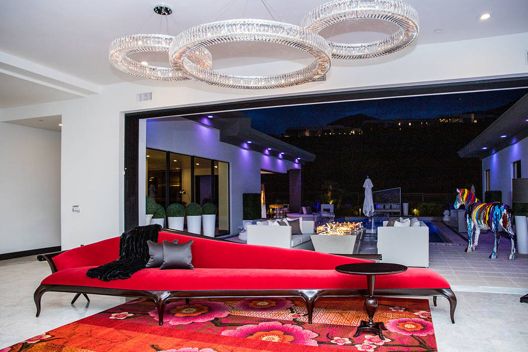 A 20-foot-long, deep-red chase lounge stretches under three ring-shaped crystal chandeliers in ...