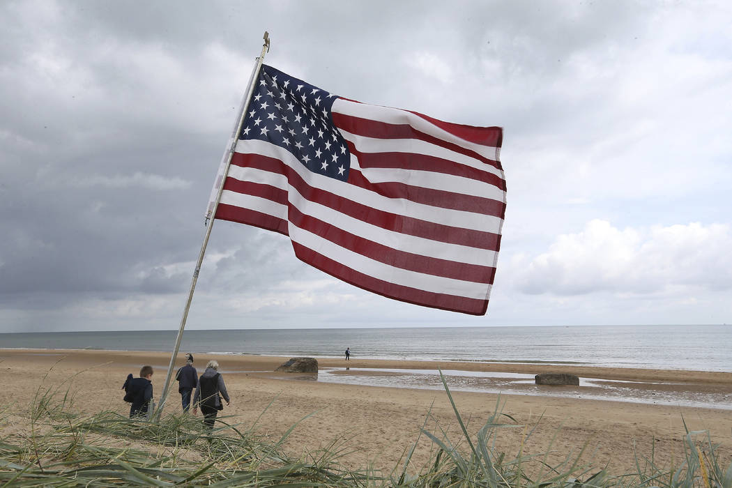 People walk on Omaha Beach, Normandy, France, where an American flag is planted, Wednesday, Jun ...