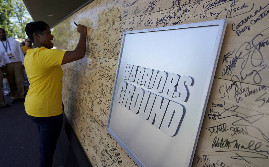 A Golden State Warriors fan signs an old piece of the basketball floor outside of Oracle Arena ...