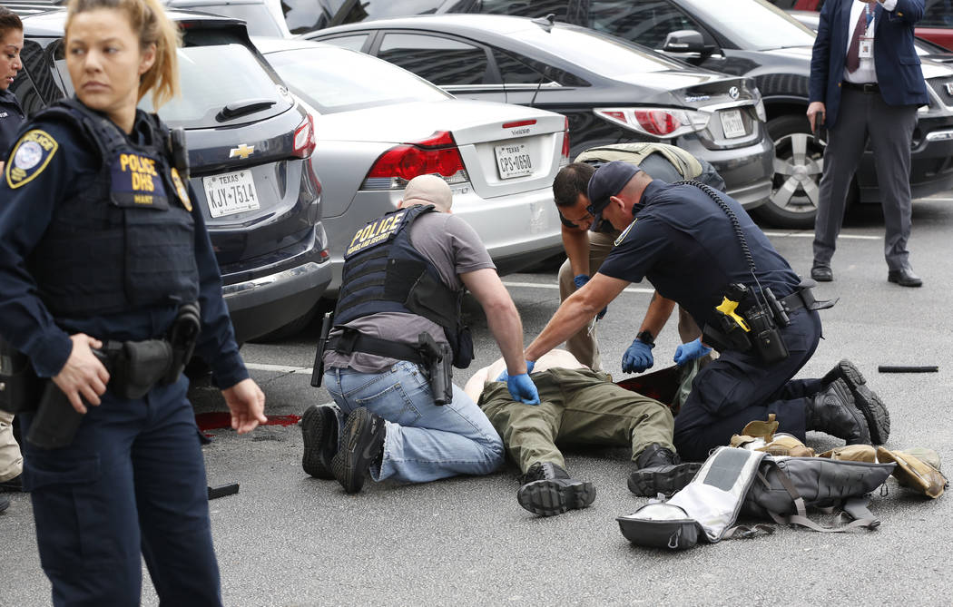 Law enforcement officers attend to an injured shooter in a parking lot after he fired shots at ...