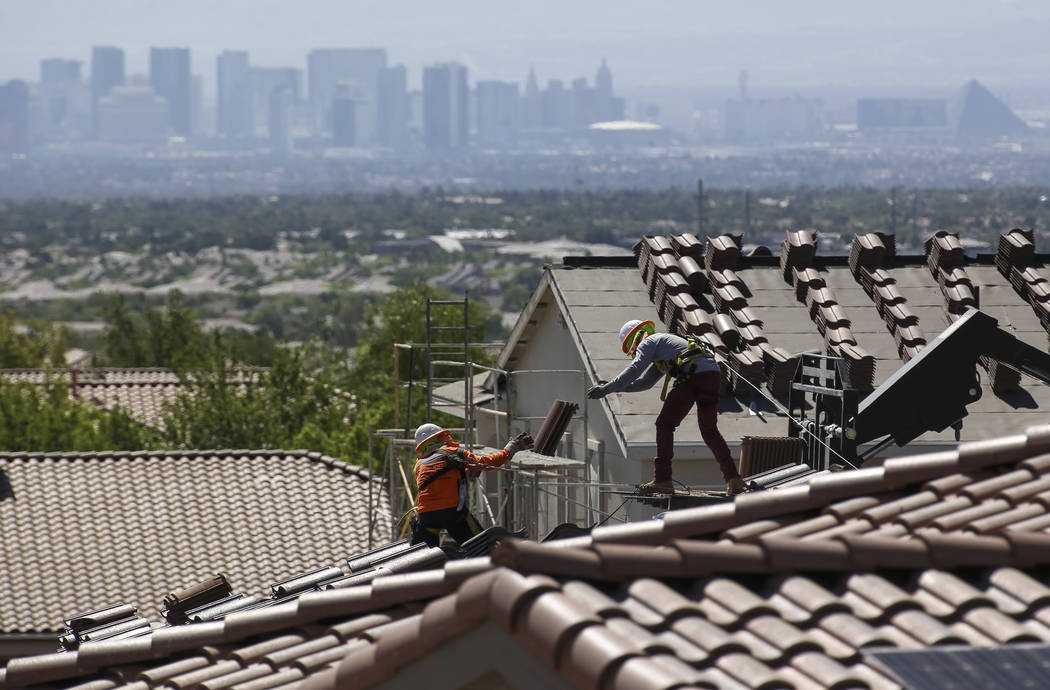 Construction workers set bundles of tile on the roof of an under-construction house in Summerli ...