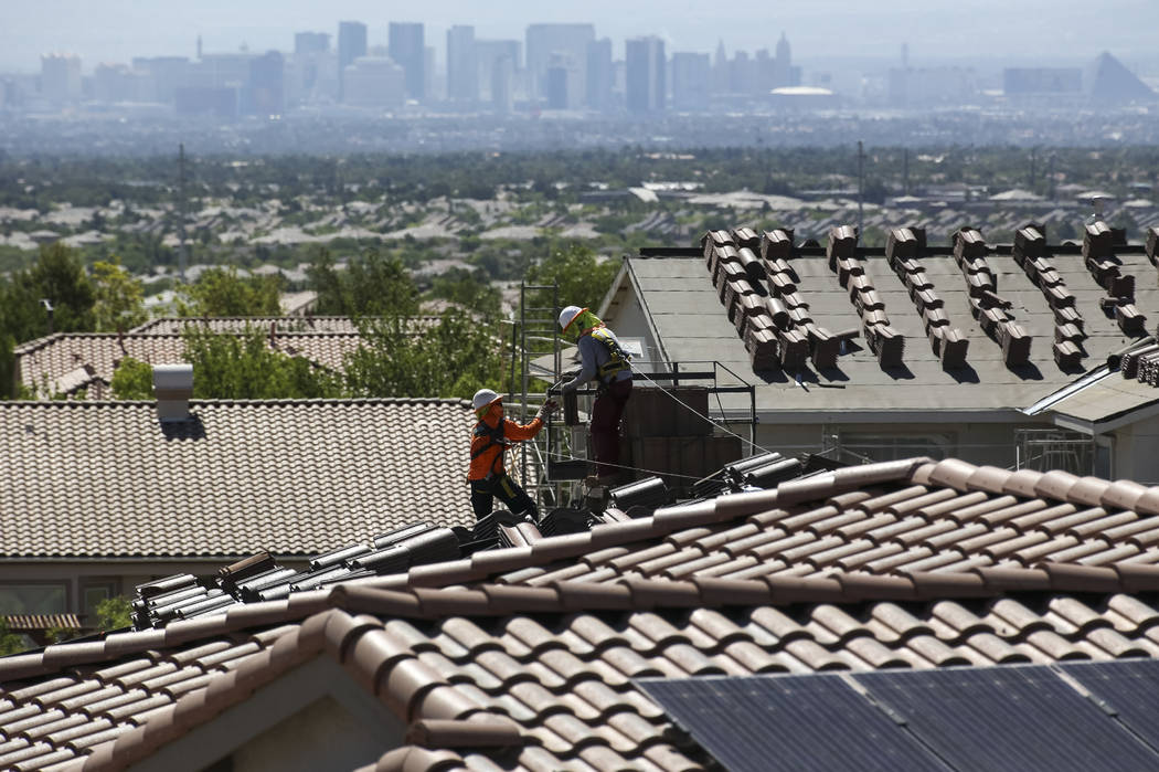 Construction workers set bundles of tile on the roof of an under-construction house in the mast ...