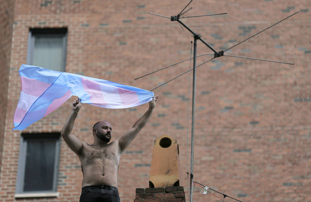 A man waves a transgender pride flag as the Queer Liberation March passes below in New York, Su ...