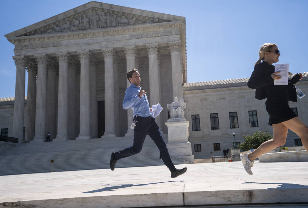 News agency interns sprint across the plaza at the Supreme Court with copies of the justices' f ...