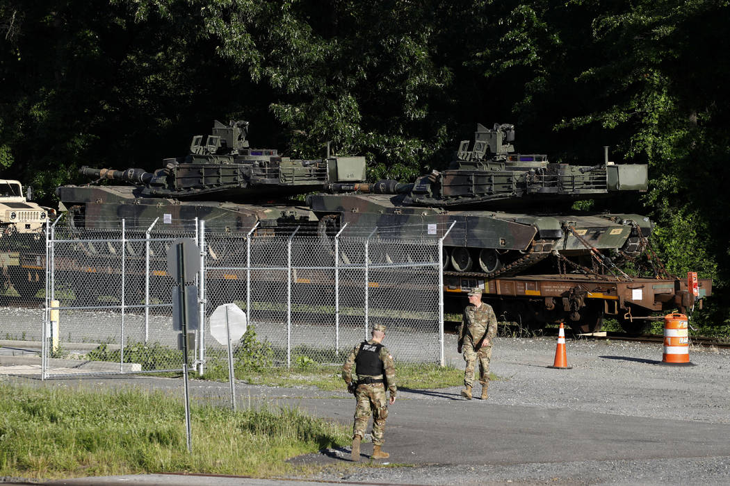 Military police walk near Abrams tanks on a flat car in a rail yard, Monday, July 1, 2019, in W ...