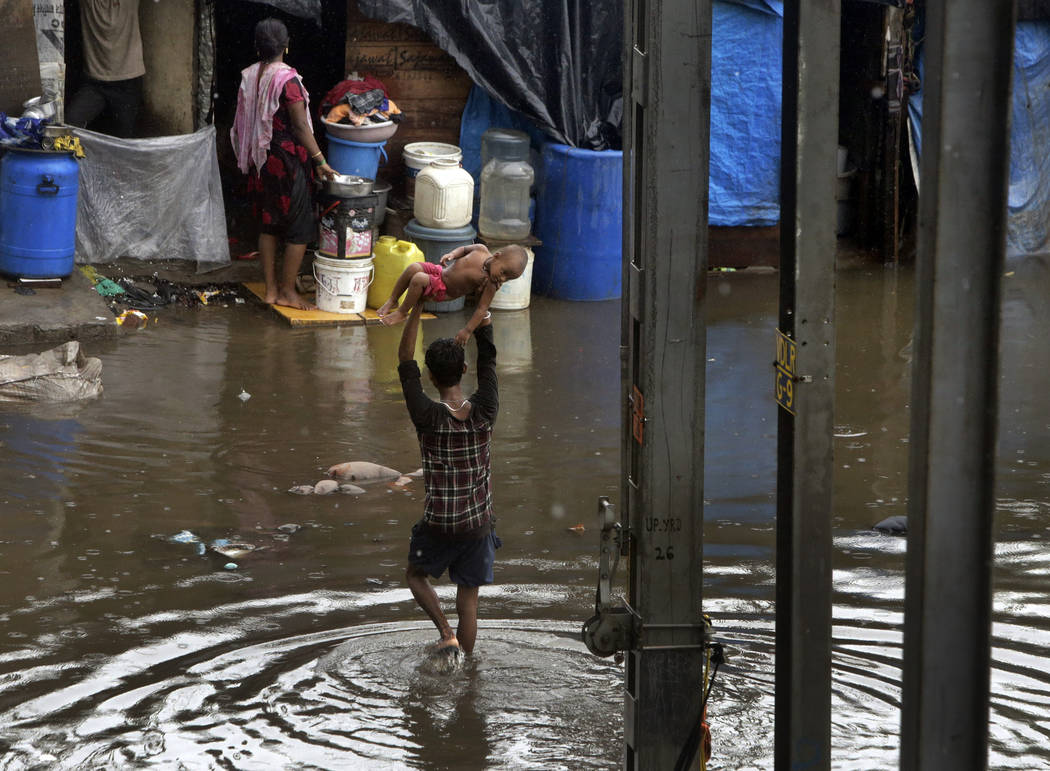 A man holds a child high above his head as he wades through a waterlogged street following heav ...