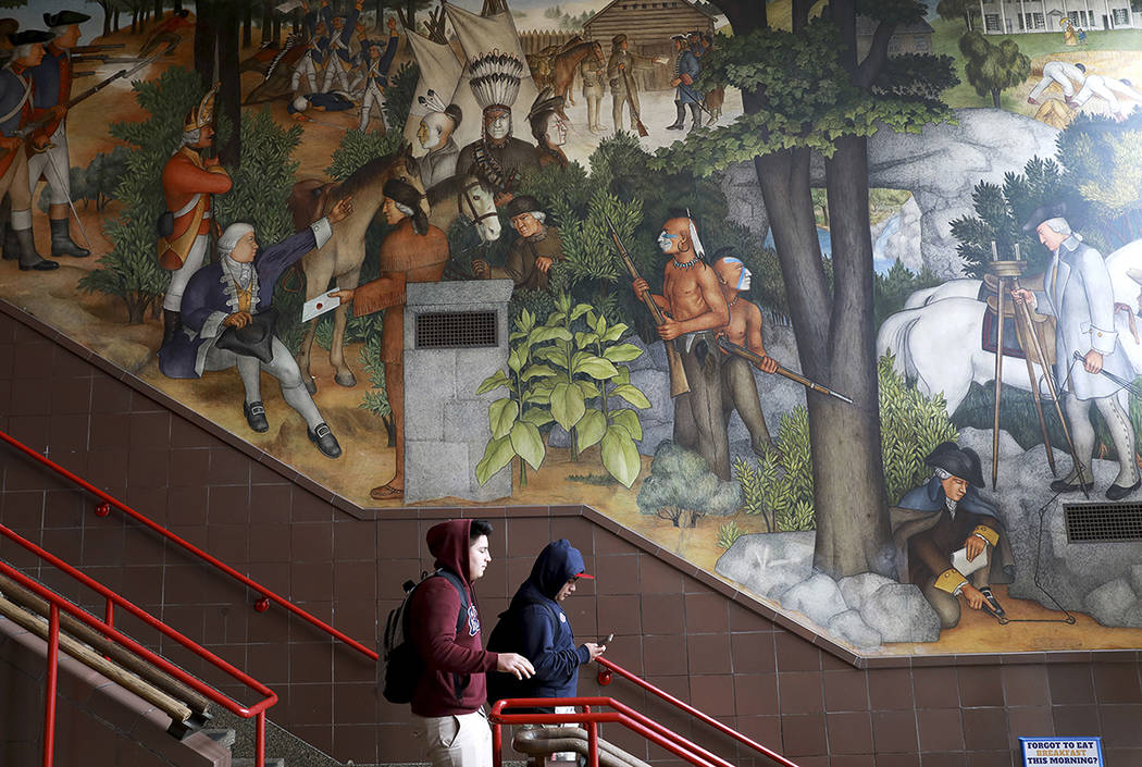 In this photo taken April 3, 2019, a pair of students walk past a historic mural that includes ...