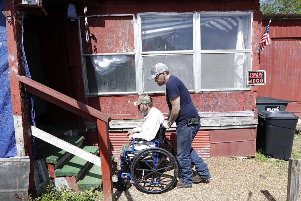 In this April 16, 2019, photo, Johnny Gibbs helps his disabled father, Mike, 65, into their hom ...