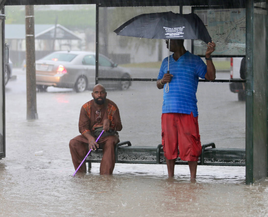 Residents sit under a bus shelter along a flooded Broad Street as heavy rain falls, Wednesday, ...