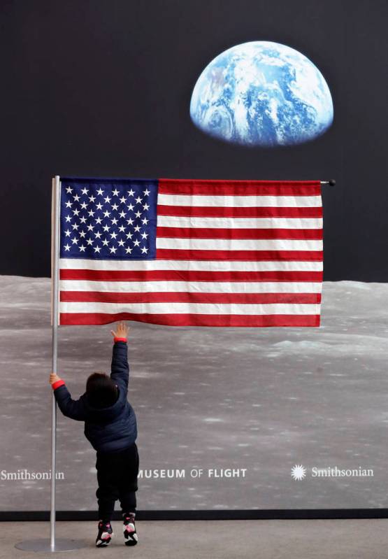 Guo JiuLe, 2, of Shanghai, China, reaches for a U.S. flag at the entrance of Destination Moon: ...