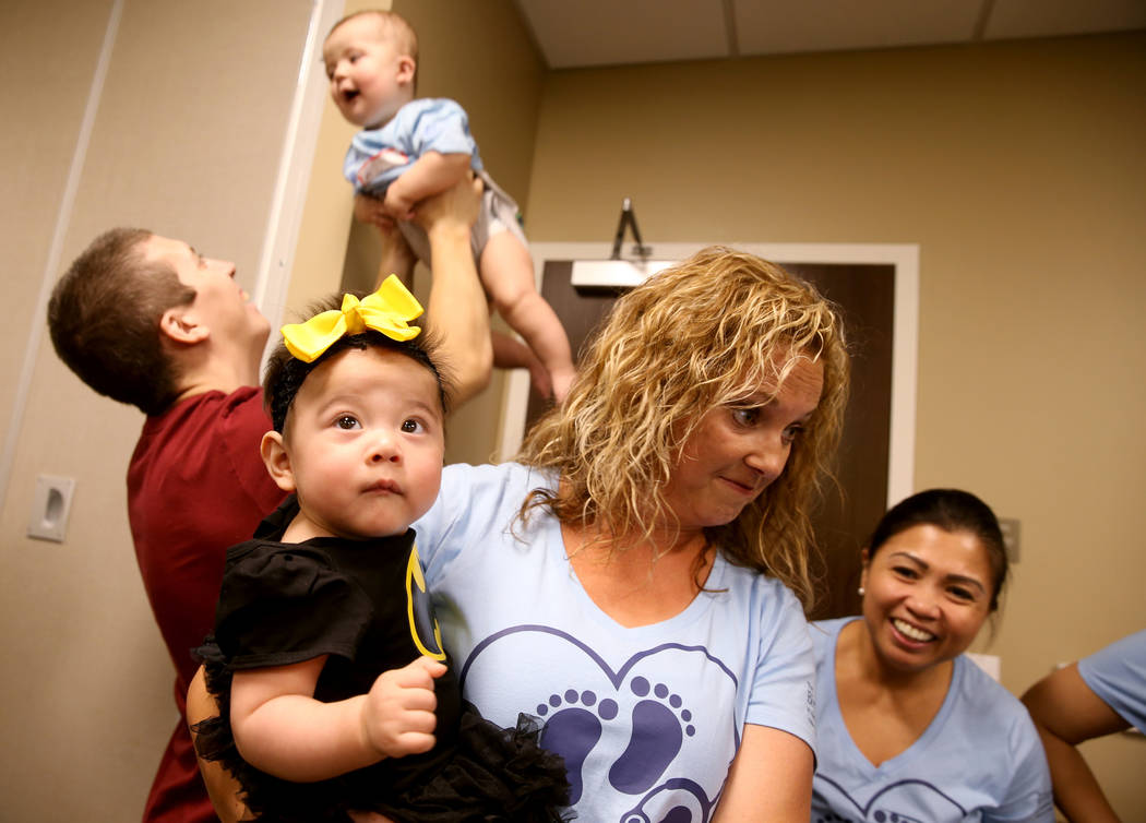 Registered Nurse Autumn Perdu holds Luna Rivas, 3 months, as Nathan Martin plays with his son, ...