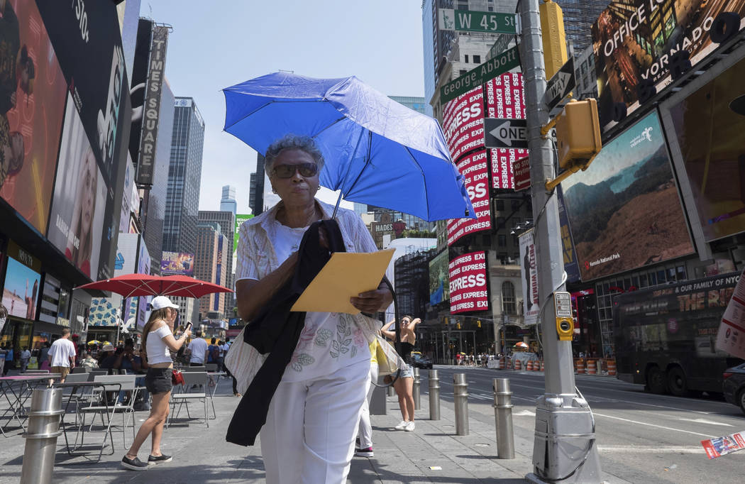 A woman uses an umbrella to block out the sun while walking through Times Square, Saturday, Jul ...